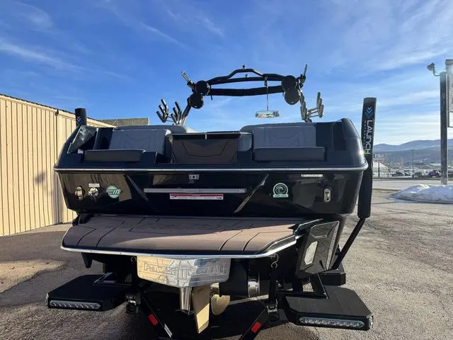Slide: The Image of 2025 Malibu 25 LSV boat, rear view, parked outdoors under clear blue sky. - 7