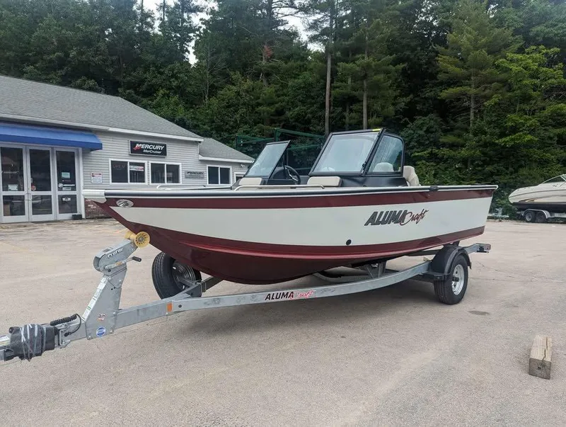 Slide: The Image of 2024 Alumacraft Trophy 185 boat on trailer, parked outdoors near dealership. - 6