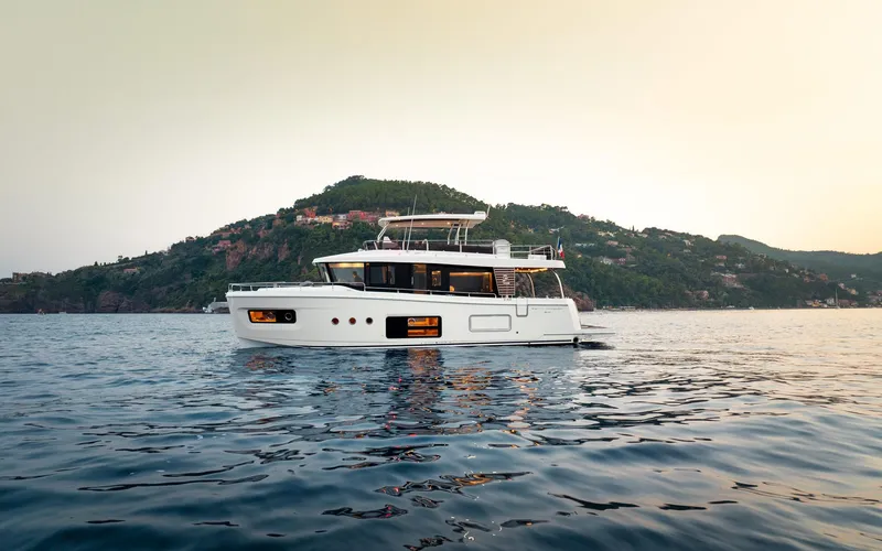 Slide: The Image of 2026 Beneteau Swift Trawler 54 cruising on serene waters with scenic hillside backdrop. - 5