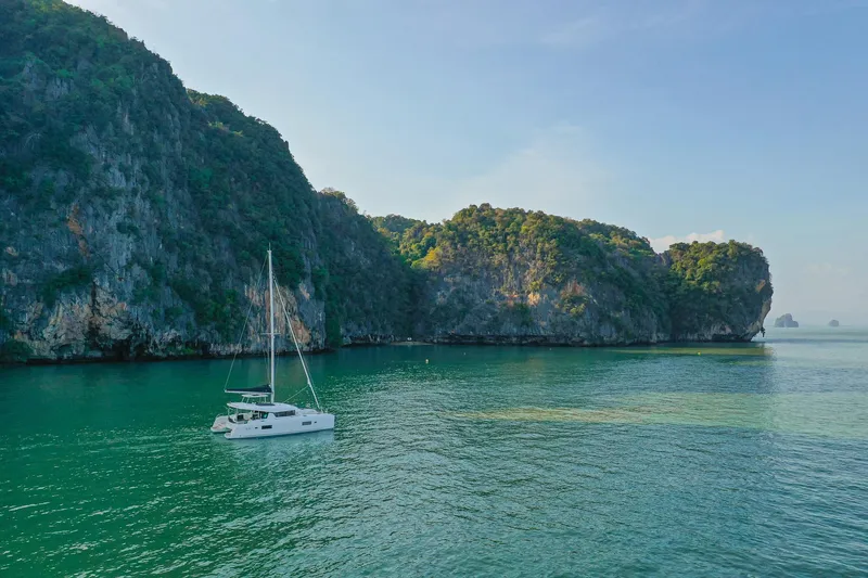 Slide: The Image of Sailing Lagoon 42 Millenium catamaran in serene turquoise waters near lush cliffs, 2025 model. - 3