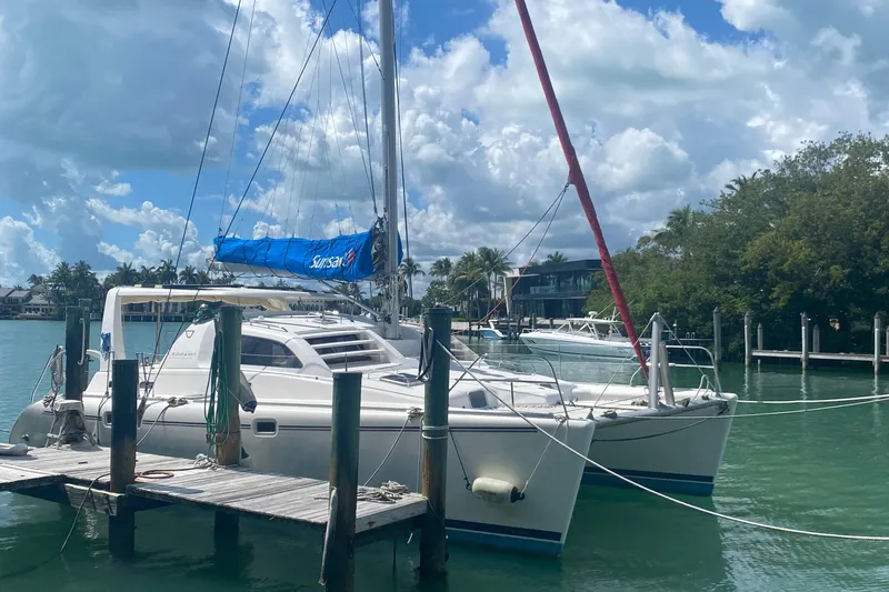 Slide: The Image of 2003 Leopard 38 catamaran docked in a serene marina under a partly cloudy sky. - 1