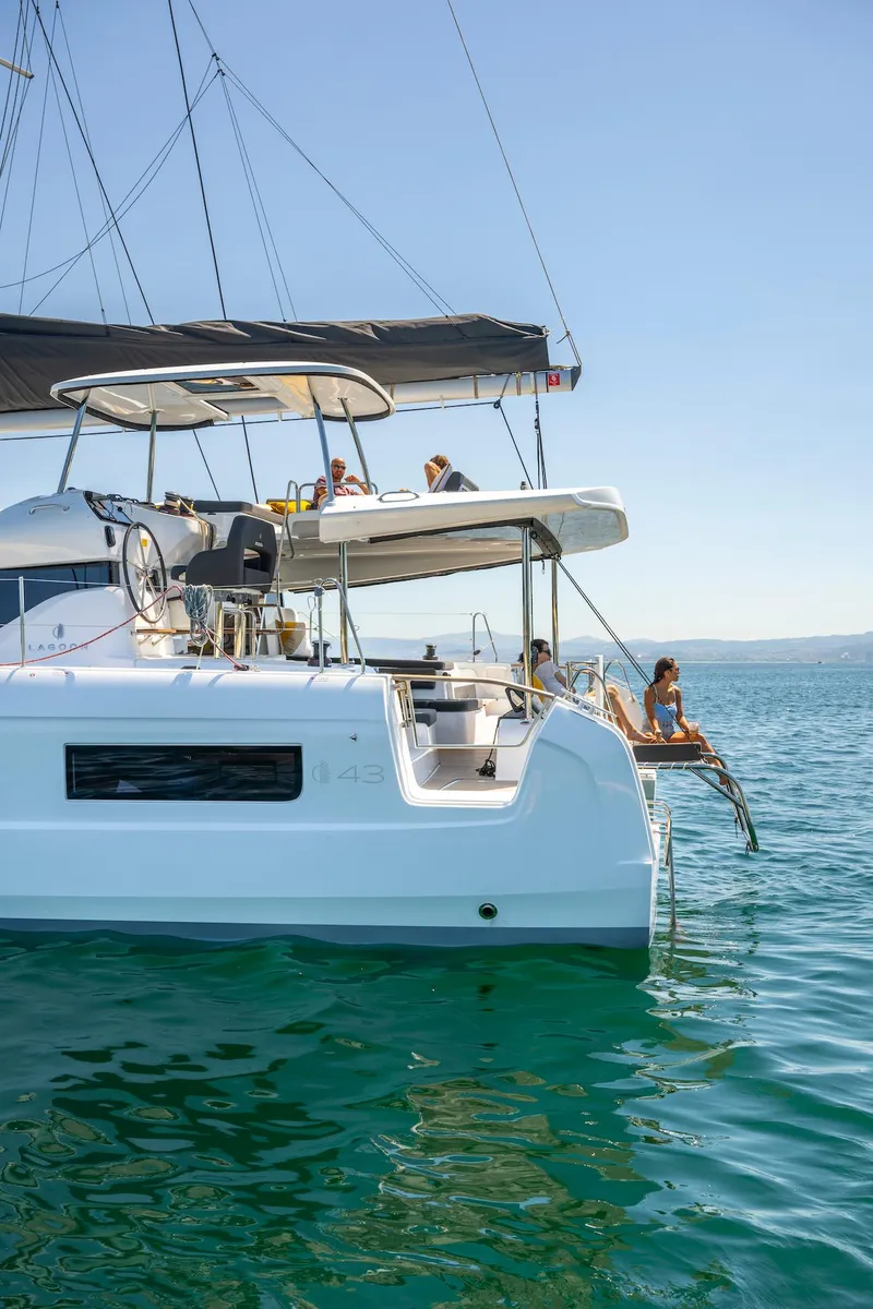Slide: The Image of 2025 Lagoon 43 catamaran sailing on clear blue waters, with people relaxing onboard. - 9