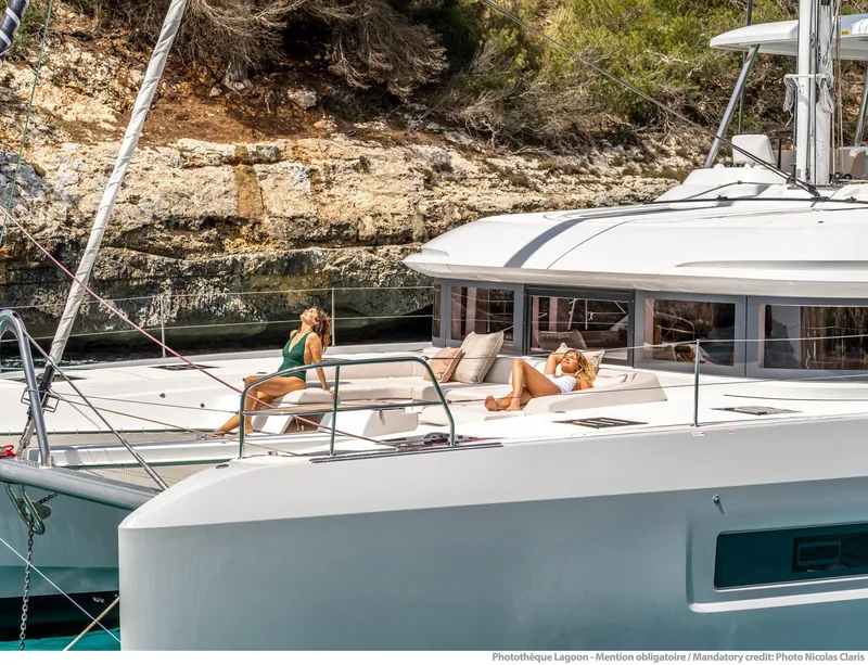 Slide: The Image of 2025 Lagoon 55 yacht with people relaxing on deck, anchored near rocky shoreline. - 9