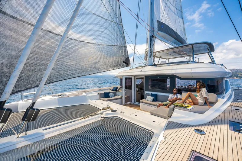 Slide: The Image of 2025 Lagoon 60 catamaran sailing with people relaxing on deck, under clear blue skies. - 11