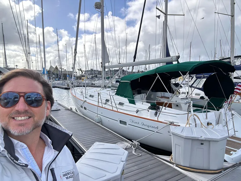 Slide: The Image of Man smiling beside a 2002 Beneteau 411 sailboat docked at a marina. - 2