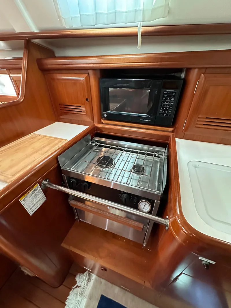 Slide: The Image of 2002 Beneteau 411 yacht kitchen with stove, oven, and microwave in wooden cabinetry. - 36