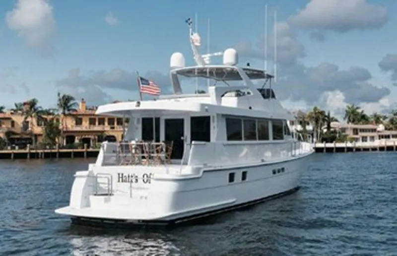 Slide: The Image of 1998 Hatteras 74 Cockpit Motor Yacht on water, with American flag, near waterfront homes. - 5