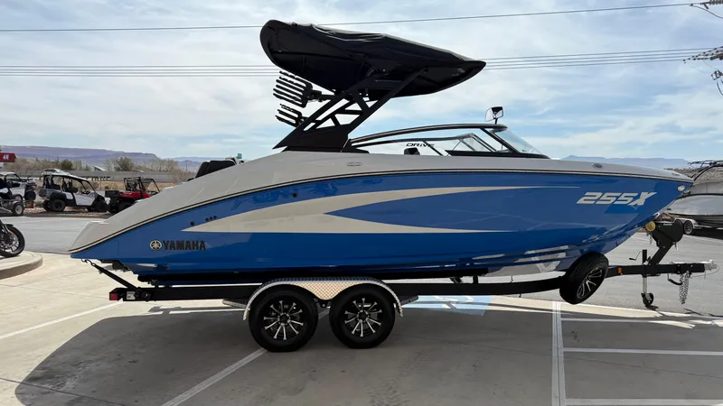 Slide: The Image of 2025 Yamaha Boats 255XD, blue and white, on a trailer in a parking lot. - 2