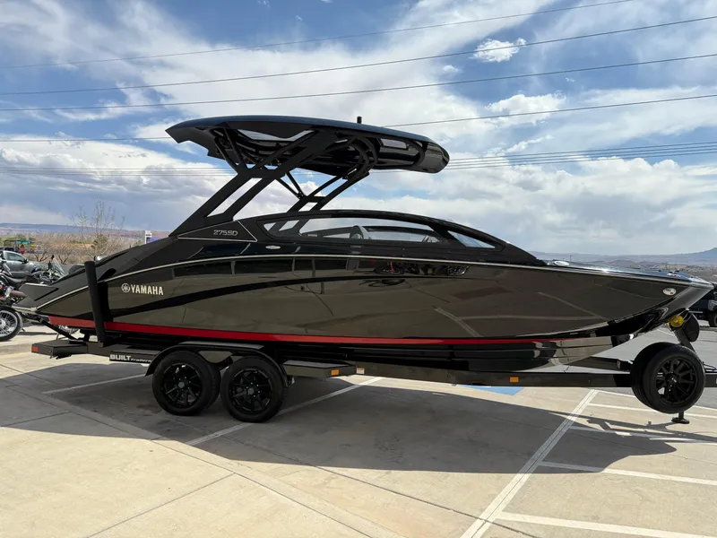 The Image of 2025 Yamaha Boats 275 SD, sleek black design, parked on a trailer under a cloudy sky. - 0