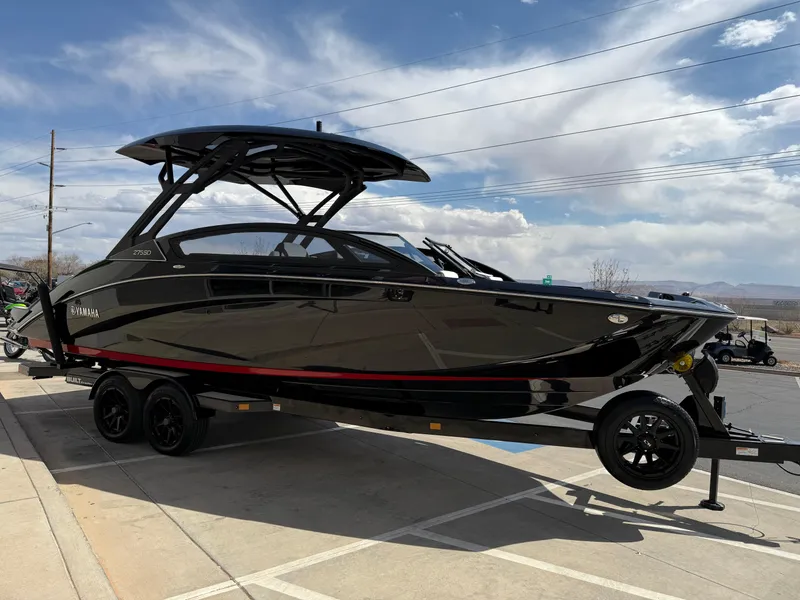 Slide: The Image of 2025 Yamaha Boats 275 SD, sleek black design, on trailer, under a partly cloudy sky. - 13