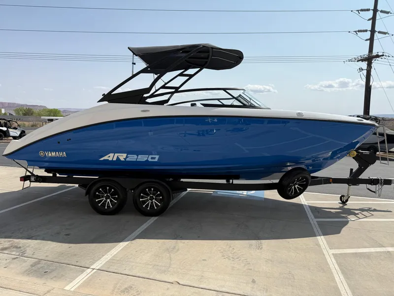 Slide: The Image of 2025 Yamaha Boats AR250, blue and white, on a trailer in a parking lot. - 10