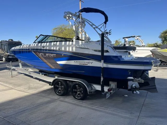 Slide: The Image of 2020 Monterey MX6 SURF boat on trailer, blue and white design, parked outdoors. - 6
