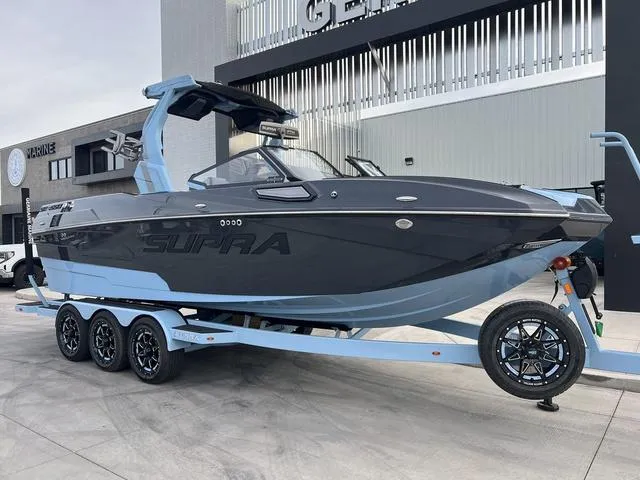 Slide: The Image of 2025 Supra SE 575 boat on trailer, sleek design, parked outdoors. - 2