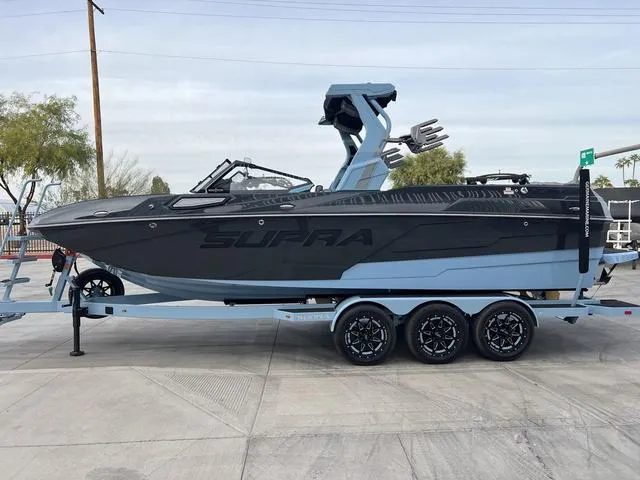 Slide: The Image of 2025 Supra SE 575 boat on trailer, sleek black and blue design, parked outdoors. - 5