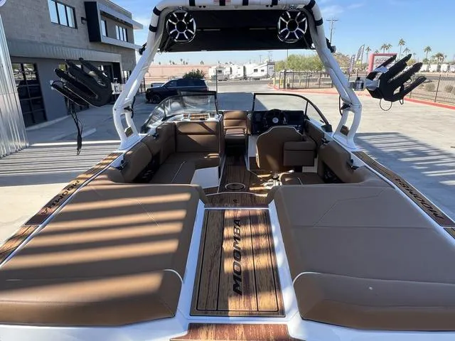 Slide: The Image of 2025 Moomba Max boat interior with tan seating and wood accents, parked outdoors. - 11