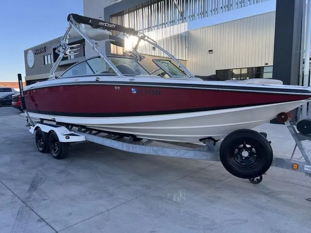 Slide: The Image of 2010 MasterCraft X45 boat on trailer, red and white, parked outside a modern building. - 2