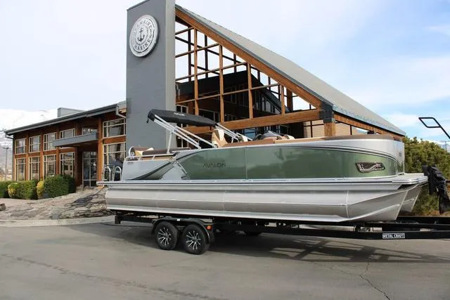 Slide: The Image of Avalon 2025 LSV Quad Lounger Shift pontoon boat on trailer, parked outside modern building. - 1