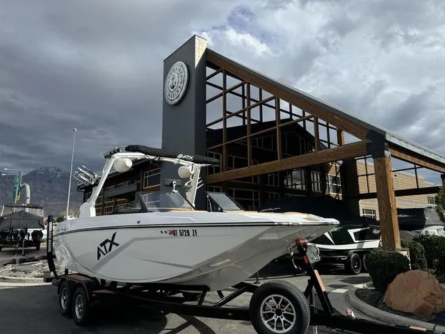 Slide: The Image of 2023 ATX Boats 22 TYPE-S on trailer, parked outside a modern building under cloudy skies. - 2