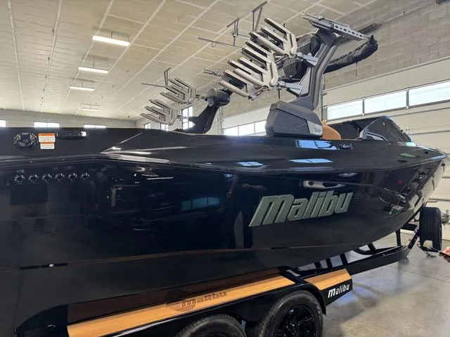 Slide: The Image of 2024 Malibu 26 LSV boat in showroom, sleek black design with advanced wakeboard racks. - 11