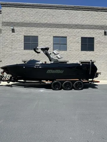 Slide: The Image of 2024 Malibu 26 LSV boat on trailer, parked outside a brick building. - 13