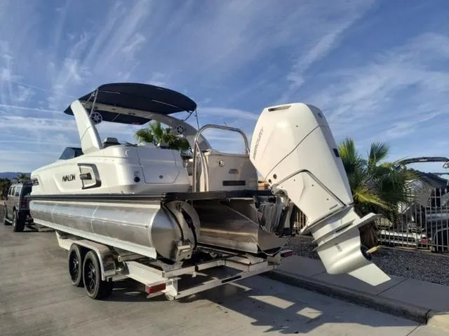 Slide: The Image of 2025 Avalon Excalibur Quad Lounge Windshield 27 FT boat on trailer, sunny day. - 4