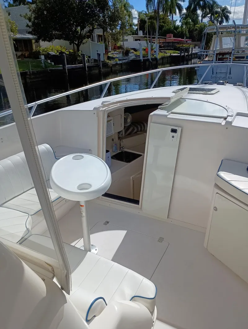 Slide: The Image of 1998 Intrepid 356 Center Console Cuddy boat interior with seating and table, docked by a canal. - 11