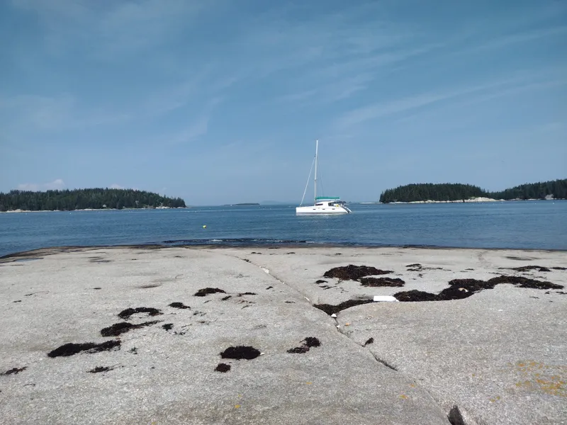 Slide: The Image of Sailboat Nautitech 402 (2011) anchored near rocky shore, clear blue sky, and calm sea. - 2