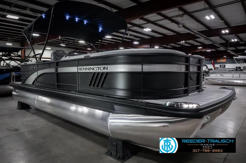 Slide: The Image of 2025 Bennington 23 LPD pontoon boat in showroom, featuring sleek black design and modern lighting. - 6