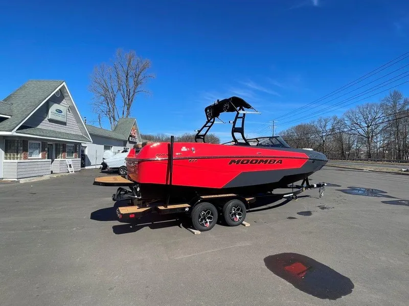 Slide: The Image of 2025 Moomba Max boat in red, parked on a trailer in a sunny outdoor setting. - 2