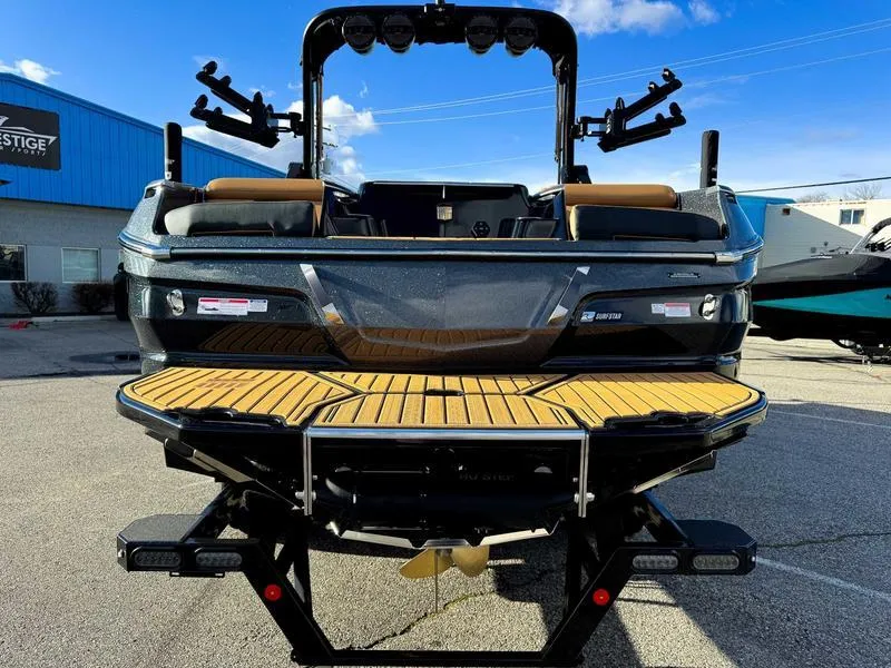 Slide: The Image of 2025 MasterCraft X24 boat with teak deck, parked outdoors under a clear blue sky. - 7