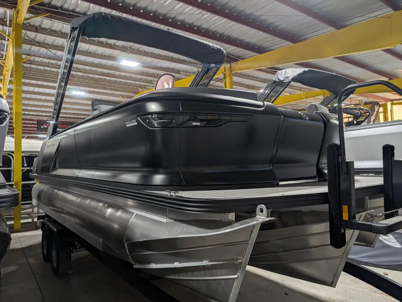 Slide: The Image of 2025 Manitou Explore pontoon boat in a showroom, featuring sleek black design and modern structure. - 2