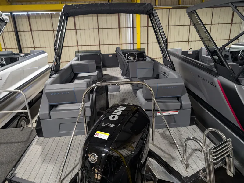 Slide: The Image of 2025 Manitou Explore boat interior with seating and motor, showcased in a showroom. - 3