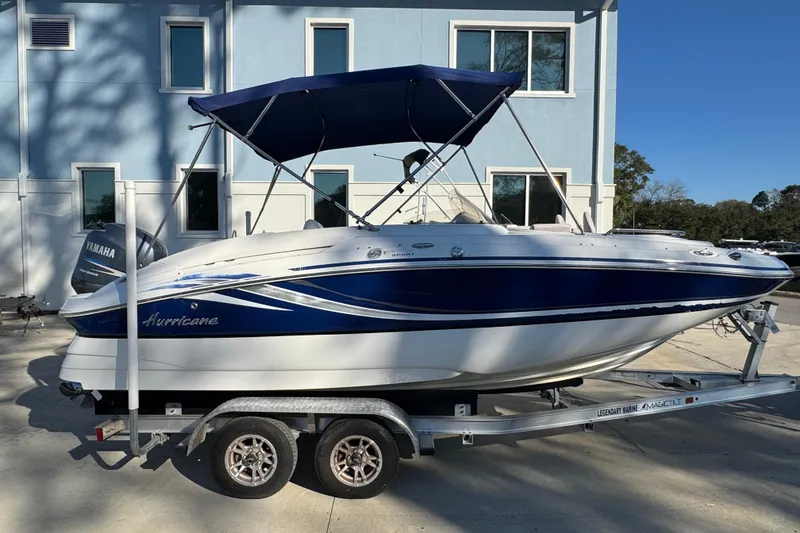 The Image of 2012 Hurricane SunDeck Sport 200 OB boat on trailer, blue and white design, parked outdoors. - 0