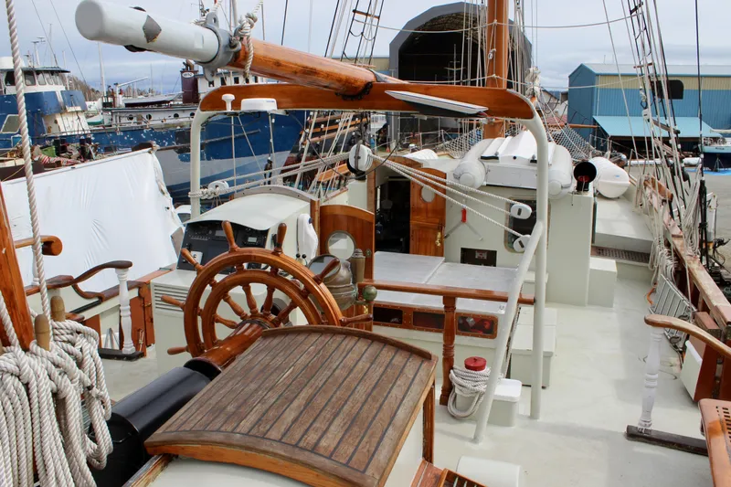 Slide: The Image of 1988 Custom Lahaina Welding Co. Square Topsail Ketch docked, showcasing wooden deck and steering wheel. - 32