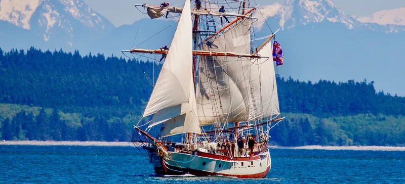 Slide: The Image of A 1988 Custom Lahaina Welding Co. Square Topsail Ketch sailing with mountains in the background. - 3