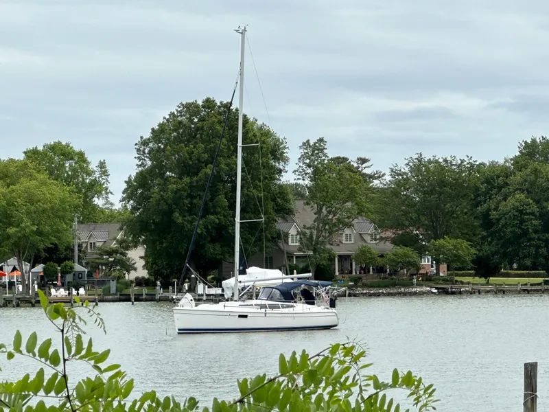 Slide: The Image of Sailboat Hunter e36 2011 on a serene lake with lush greenery and houses in the background. - 11