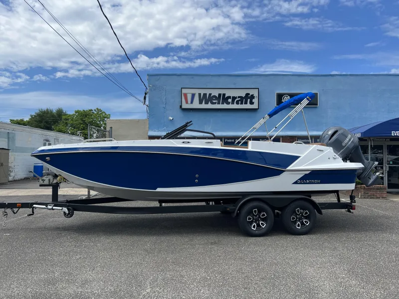 The Image of 2023 Glastron GTD 220 boat on trailer, blue and white design, parked outside dealership. - 0