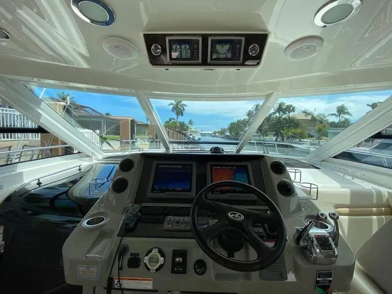 Slide: The Image of 2010 Sea Ray 540 Sundancer helm with navigation screens and steering wheel, overlooking a scenic waterway. - 2