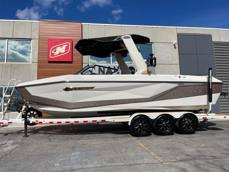 Slide: The Image of 2025 Nautique Super Air Nautique G25 boat on trailer, parked outside a building. - 1