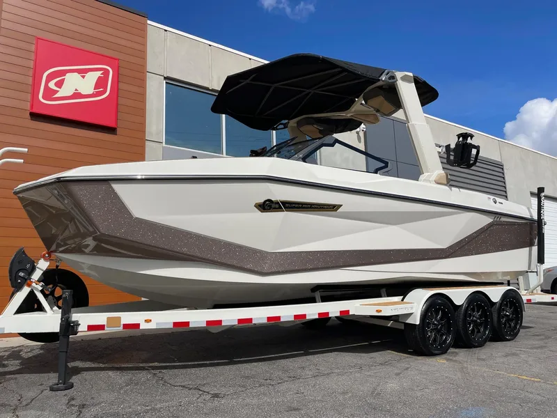 Slide: The Image of 2025 Nautique Super Air Nautique G25 boat on trailer, parked outside a building. - 2