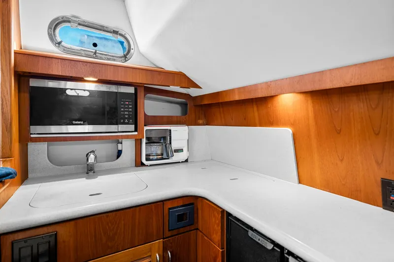 Slide: The Image of 2002 Pursuit 3800 Express yacht kitchen with microwave, coffee maker, and wooden cabinetry. - 31