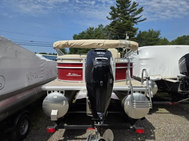 Slide: The Image of 2025 Sun Tracker PB 20 DLX pontoon boat with Mercury outboard motor, parked outdoors. - 6