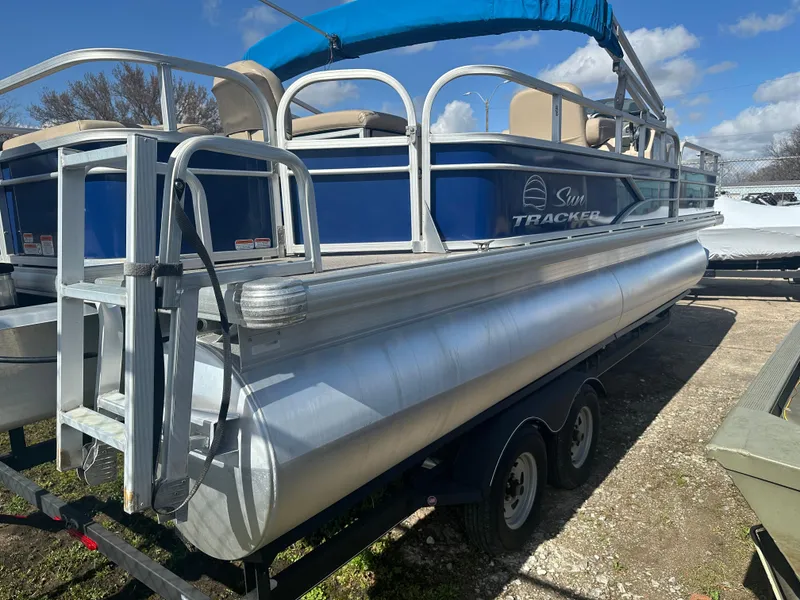 Slide: The Image of 2017 Sun Tracker Fishin' Barge 22 DLX pontoon boat on trailer, blue and silver design. - 5