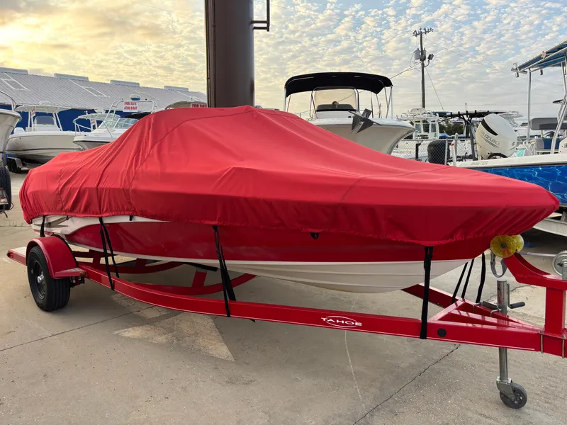 Slide: The Image of 2011 Tracker Tahoe Q5i boat with red cover on trailer, docked outdoors. - 2