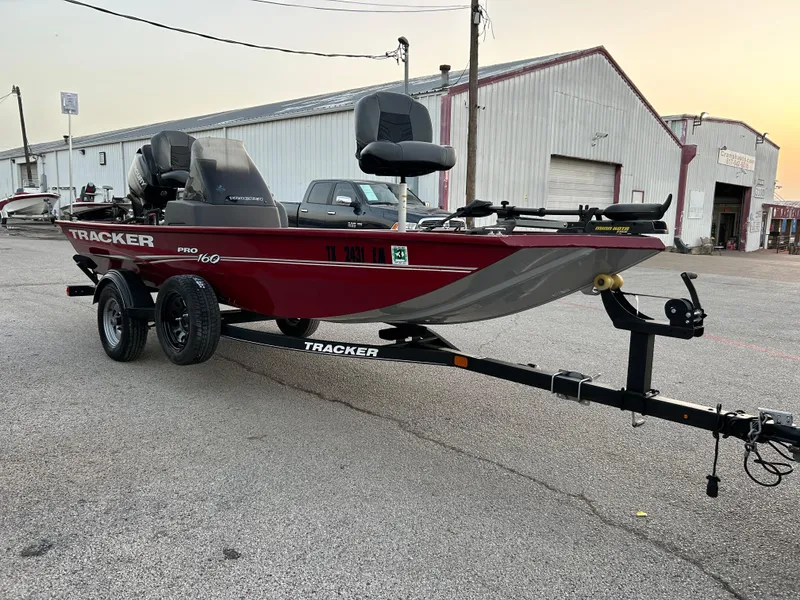 Slide: The Image of 2019 Tracker Pro 160 boat on trailer, parked outdoors near industrial building. - 2
