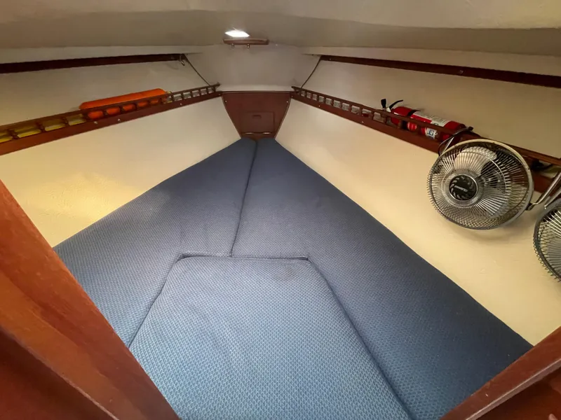 Slide: The Image of 1984 Catalina 30 interior cabin with blue bedding, fan, and storage shelves. - 11