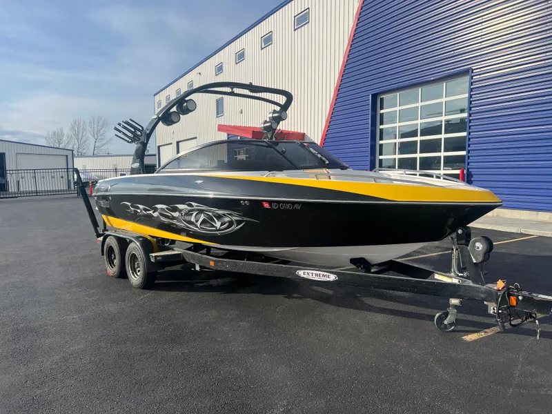 Slide: The Image of 2007 Malibu WVLX boat on trailer, black and yellow design, parked outside industrial building. - 3