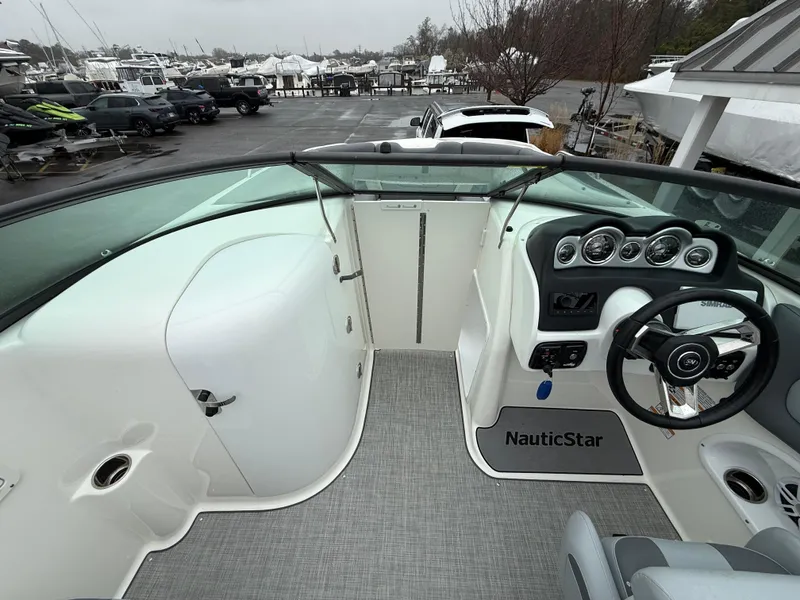 Slide: The Image of 2024 NauticStar 243 DC Deck boat interior with steering wheel and dashboard, docked at marina. - 14