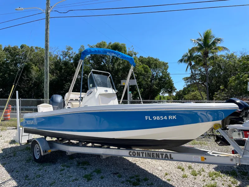 The Image of 2017 Robalo 206 Cayman boat on trailer, blue hull, parked outdoors. - 1