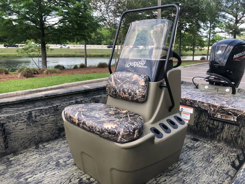 Slide: The Image of 2025 Tracker Grizzly 1860 CC boat with camo seats and console, near a scenic lake. - 10